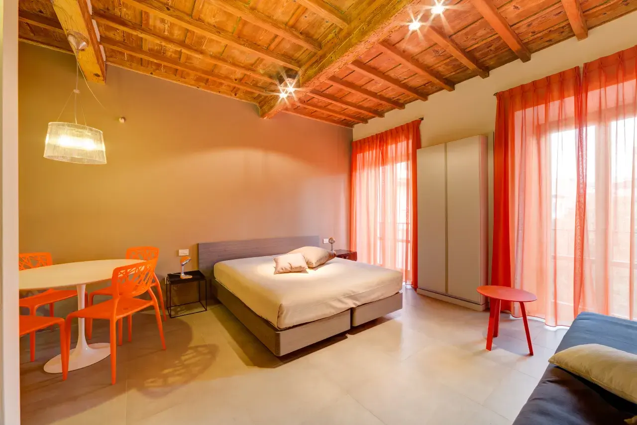 General view of a Mono Smart apartment featuring a double bed in the background and a dining table with 4 chairs.